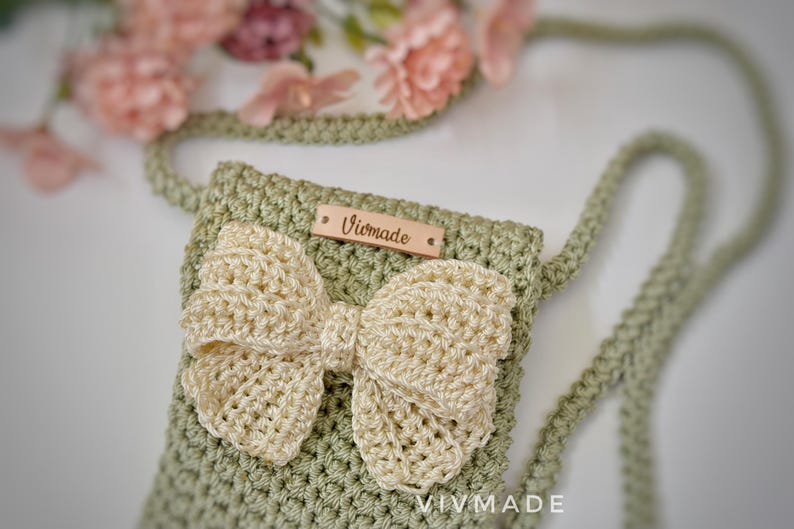 May include: A green crocheted bag with a white crocheted bow and a wooden tag that says "Vivmade".