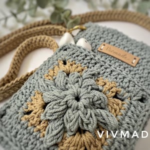 May include: A crocheted bag in a light blue and tan colour scheme. The bag features a flower design and a leather tag that reads "Vivmade".