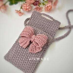 May include: A gray crocheted phone pouch with a pink crocheted bow. The pouch has a strap and the text "VIVMADE" is visible on the front.