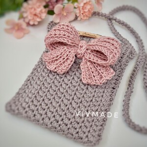 May include: A small crocheted bag with a pink bow and a long strap. The bag has the text "VIVMADE" on the front.