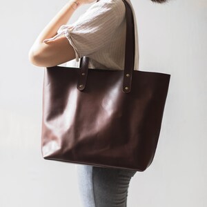 May include: A brown leather tote bag with two straps and brass accents. The bag is large enough to carry everyday essentials.