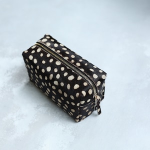 May include: A black and white polka dot makeup bag with a gold zipper.