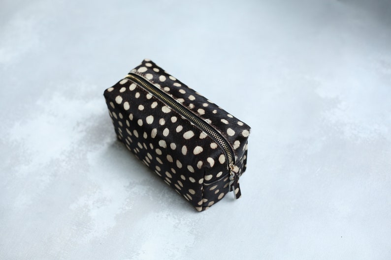 May include: A black and white polka dot makeup bag with a gold zipper.