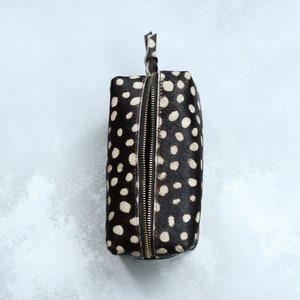 May include: A black and white polka dot makeup bag with a gold zipper.