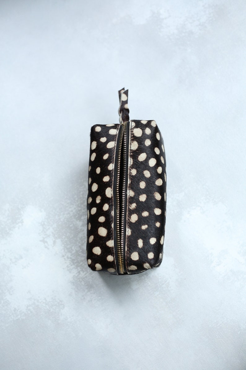 May include: A black and white polka dot makeup bag with a gold zipper.