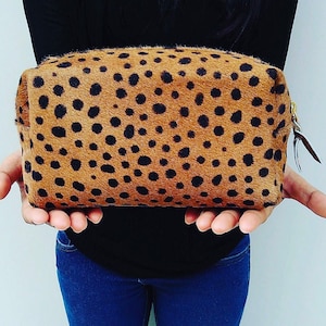 May include: A brown and black spotted cosmetic bag with a gold zipper.