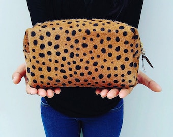 May include: A brown and black spotted cosmetic bag with a gold zipper.