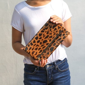 May include: A brown and black leopard print clutch purse with a gold zipper.