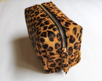 May include: A small, rectangular leopard print makeup bag with a gold zipper.