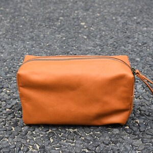 Könnte beinhalten: Eine braune Leder-Reisetasche mit Reißverschluss und Tragegriff.