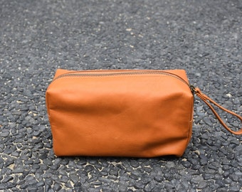 May include: A brown leather travel bag with a zipper closure and a handle.