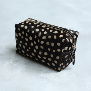 May include: A black and white polka dot makeup bag with a gold zipper.