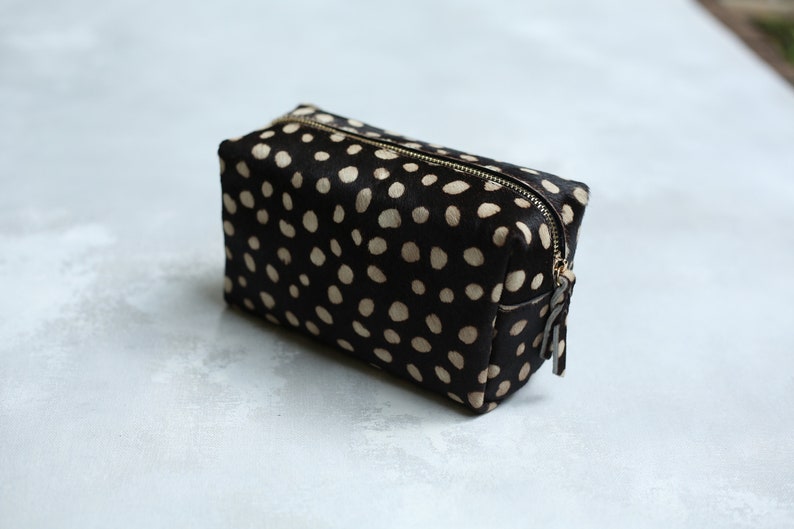 May include: A black and white polka dot makeup bag with a gold zipper.