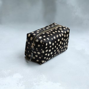 May include: A black and white polka dot makeup bag with a gold zipper.