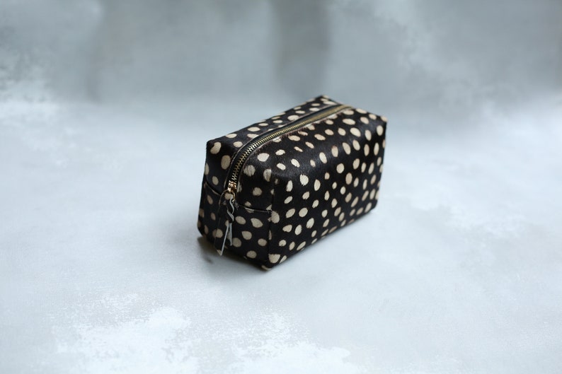 May include: A black and white polka dot makeup bag with a gold zipper.