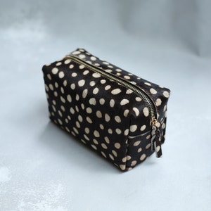 May include: A black and white polka dot makeup bag with a gold zipper.