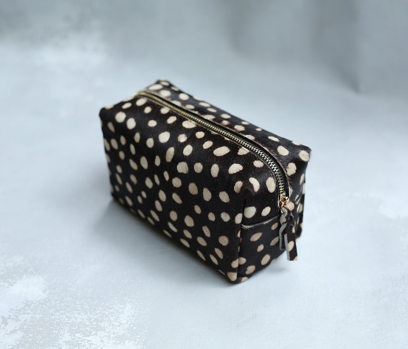 May include: A black and white polka dot makeup bag with a gold zipper.