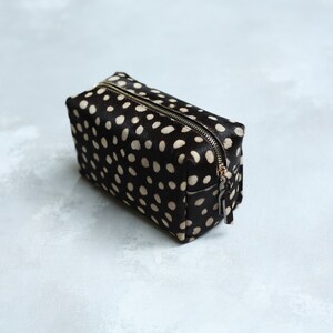 May include: A black and white polka dot makeup bag with a zipper closure.