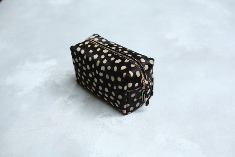 May include: A black and white polka dot makeup bag with a zipper closure.