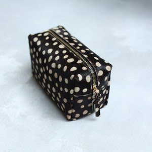 May include: A black and white polka dot makeup bag with a gold zipper.