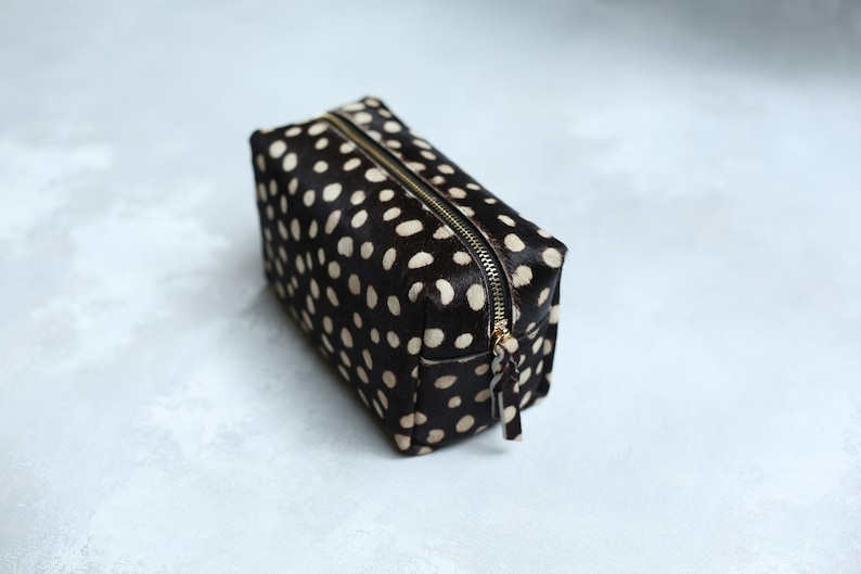 May include: A black and white polka dot makeup bag with a gold zipper.