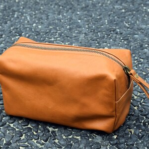 May include: A brown leather travel toiletry bag with a zipper closure and a leather strap.