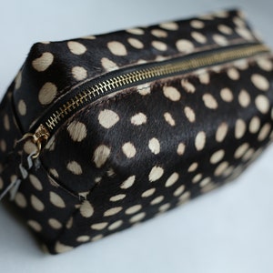 May include: A black and white spotted toiletry bag with a gold zipper.