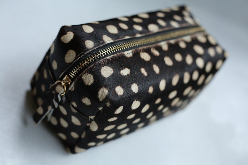May include: A black and white spotted toiletry bag with a gold zipper.