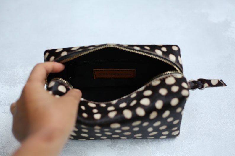 May include: A black and white polka dot makeup bag with a brown leather zipper pull and a gold zipper. The bag is open and the inside is black.