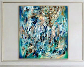 Puede incluir: Pintura abstracta de gran formato con marco dorado, con pinceladas azules, turquesas, marrones y doradas. Cuelga sobre un sofá blanco con cojines dorados y azul marino. Una mesa de centro blanca y un jarrón decorativo completan la escena.