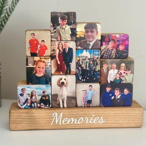 Peut inclure: Une tour de blocs en bois avec des photos d'une famille imprimées sur chaque bloc. Les blocs sont empilés en forme de pyramide et la tour repose sur une base en bois avec le mot "Souvenirs" écrit dessus.