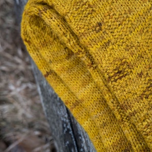 K&ouml;nnte beinhalten: Nahaufnahme einer gelben Stricksocke mit einem strukturierten Muster. Die Socke ist umgeklappt und das Garn ist sichtbar.