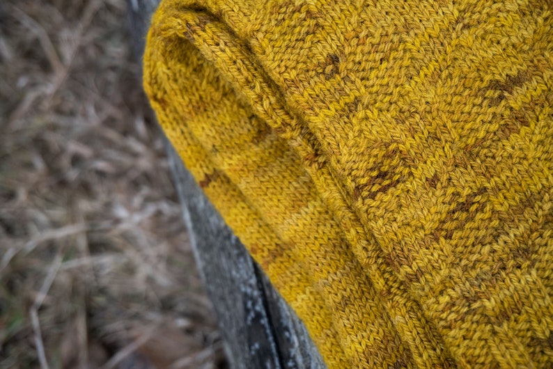 K&ouml;nnte beinhalten: Nahaufnahme einer gelben Stricksocke mit einem strukturierten Muster. Die Socke ist umgeklappt und das Garn ist sichtbar.