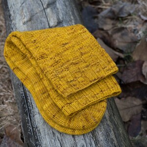 K&ouml;nnte beinhalten: Ein Paar gelbe Stricksocken mit einem strukturierten Muster. Die Socken sind gefaltet und liegen auf einer Holzoberfl&auml;che.