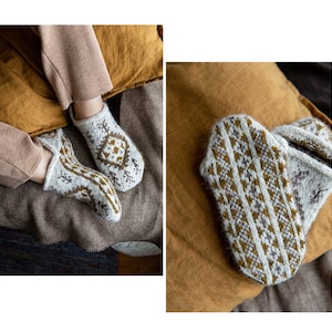 May include: A pair of white knitted socks with a brown and gray geometric pattern. The socks are lying on a brown and tan textured surface.