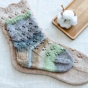 May include: Two pairs of knitted socks, one pair is a light brown with a lacy pattern and the other pair is a multi-colored sock with green, blue, and brown shades.