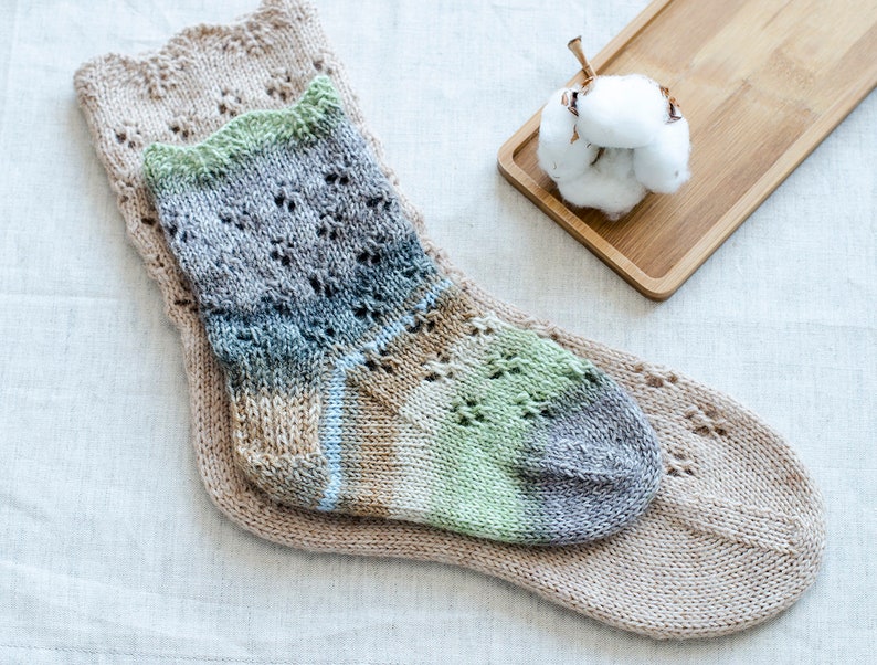May include: Two pairs of knitted socks, one pair is a light brown with a lacy pattern and the other pair is a multi-colored sock with green, blue, and brown shades.