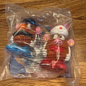 Puede incluir: Dos juguetes de Mr. Potato Head sellados en una bolsa de plástico transparente. Uno tiene un sombrero azul y el otro una pajarita roja. Los juguetes son marrones con accesorios coloridos.