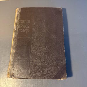May include: A vintage book with a dark cover, titled "Christian Service Songs." The book's spine and edges show signs of wear. The text is printed in a serif font. The book appears to be an old hymnal.