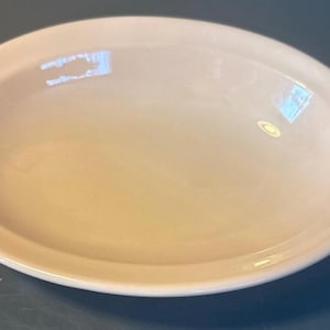 May include: A pale peach-coloured oval serving dish. The dish has a smooth, glossy surface and a slightly raised rim. The shape is ideal for serving salads, side dishes, or desserts. The dish is made of ceramic.