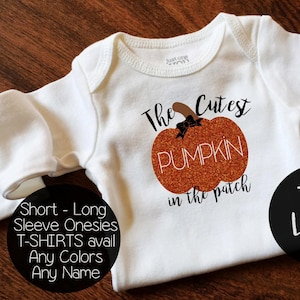 May include: White onesie with a glittery orange pumpkin and the text "The Cutest Pumpkin in the patch". The onesie is available in short or long sleeves and in any color. The text "TLC Tiny Love Co." is in the bottom right corner.