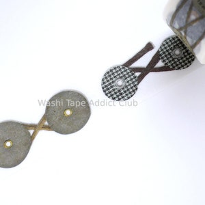 May include: A roll of decorative adhesive tape featuring a repeating pattern of circular tags connected by crisscrossed brown lines. The tags include a black and white houndstooth print, solid gray circles, and a brown circle with the number 2.