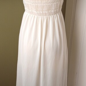 May include: A white slip dress with lace trim around the neckline and hem. The dress has a fitted bodice and a flowing skirt.
