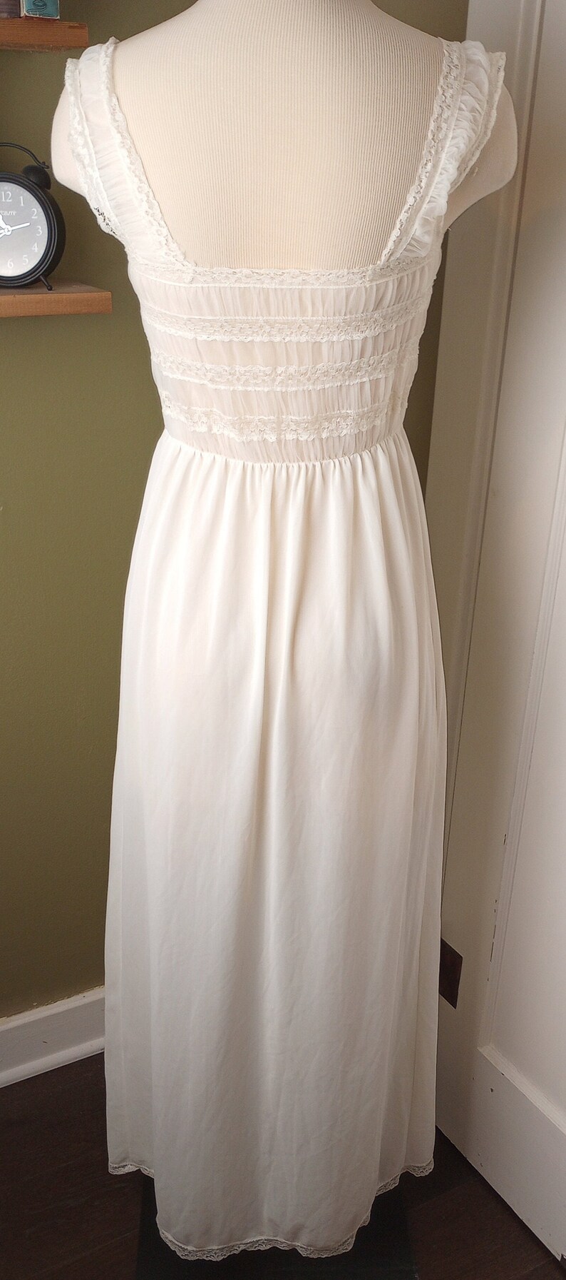 May include: A white slip dress with lace trim around the neckline and hem. The dress has a fitted bodice and a flowing skirt.