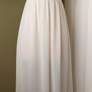 May include: A white lace and chiffon slip dress with a fitted bodice and a flowing skirt. The dress has a lace trim around the neckline and the hem.
