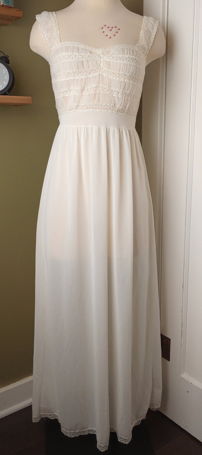 May include: A white lace and chiffon slip dress with a fitted bodice and a flowing skirt. The dress has a lace trim around the neckline and the hem.