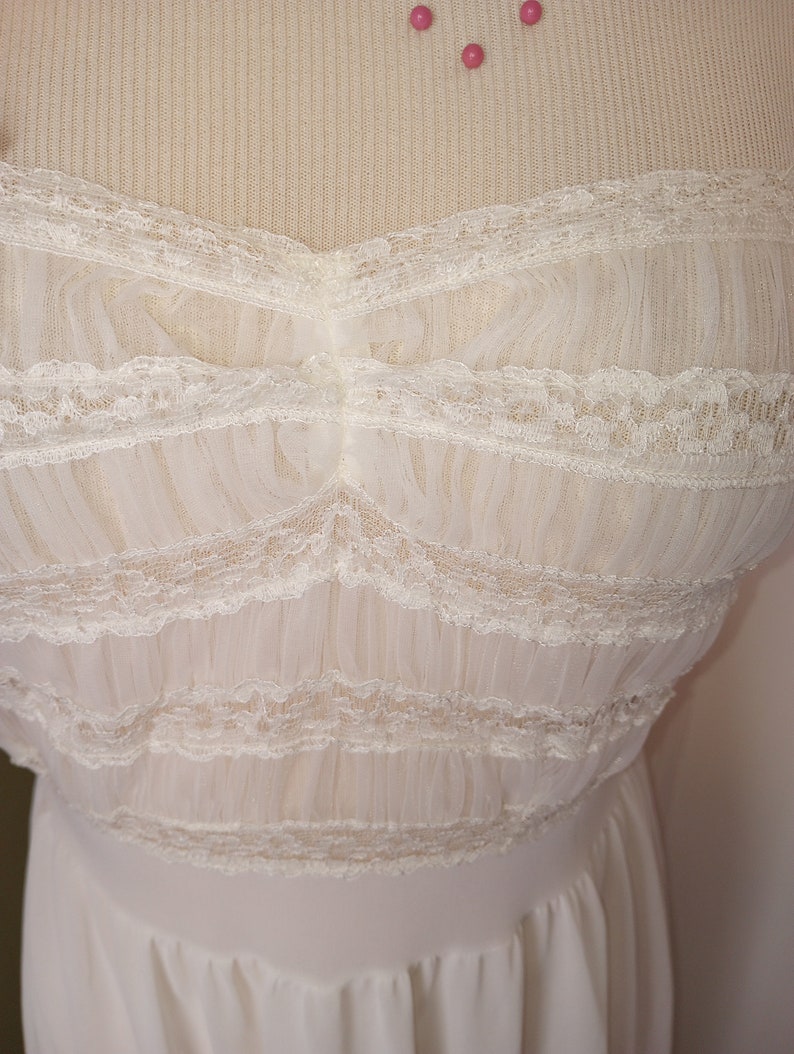 May include: A white lace and tulle dress with a sweetheart neckline. The dress has a fitted bodice and a flowing skirt.