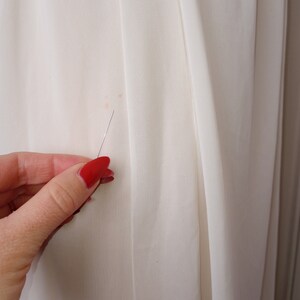 May include: Close-up of a white fabric with a small brown stain. A hand with red nail polish is holding a pin near the stain.