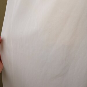 May include: White fabric with a smooth texture. The fabric is slightly wrinkled.