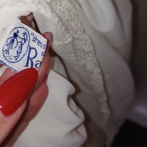 May include: White lace trim on a white garment with a blue and white label that reads "dress size R"